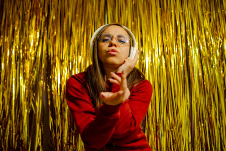 A woman wearing glasses and headphones energetically dances in front of a shimmering gold backdropの写真素材