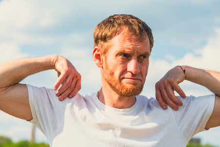 A professional sportsman in a white shirt is standing, holding his hands on his head as he performs...