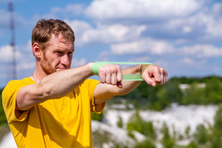 A professional sportsman in a yellow shirt is holding a Elastic band expander. He appears focused...