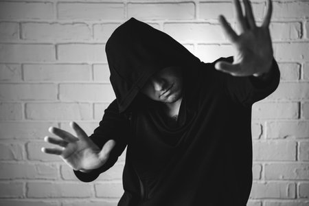 A man wearing a black hoodie is energetically dancing with expressive hand movements in front of a white brick wall.の写真素材