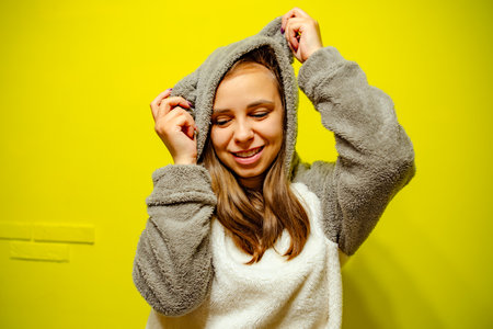 Woman in Cozy Sweater Dancing Against Bright Yellow Wall During Daytime.の写真素材