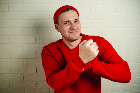 A man in a red hoodie and hat dances against a white brick wall.の写真素材