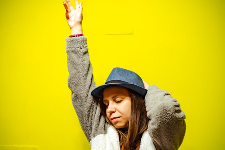 Woman in Cozy Sweater Dancing Against Bright Yellow Wall During Daytime.