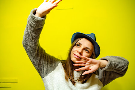 Woman in Cozy Sweater Dancing Against Bright Yellow Wall During Daytime.の写真素材