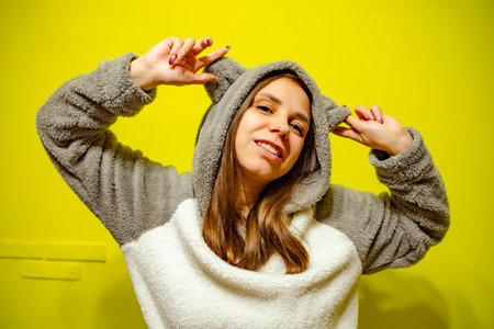 Woman in Cozy Sweater Dancing Against Bright Yellow Wall During Daytime.の写真素材