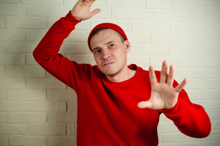 A man in a red hoodie and hat dances against a white brick wall.の写真素材