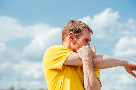 A professional sportsman is standing in front of a clear blue sky, engaging in shoulder and arm...