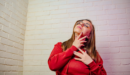 Woman Dancing Gracefully in Red Sweatshirt Against White Brick Wall at Evening.の写真素材