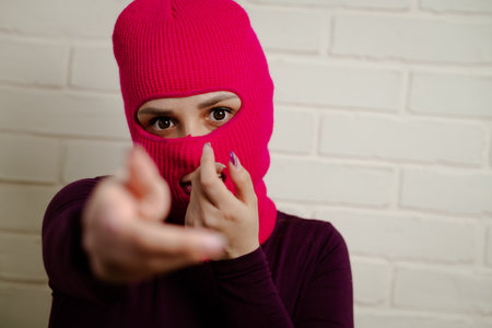 A woman wearing a bright pink balaclava dances energetically, striking unique poses with her hands against a clean, white brick wall background.の写真素材