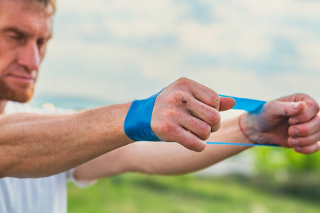 A professional sportsman in a white shirt is holding a Elastic band expander. He appears focused and determined as he prepares his shoulder and arm muscles for the workout aheadの写真素材