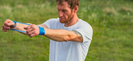 A professional sportsman in a white shirt is holding a Elastic band expander. He appears focused and...