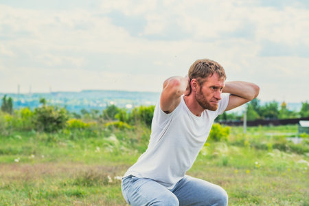 A professional sportsman is squatting in a field, with his hands behind his head. Male Performing...