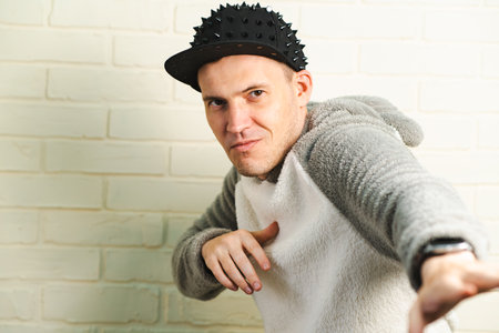 A man wearing a black cap and a gray sweater is captured in motion, dancing gracefully with fluid...