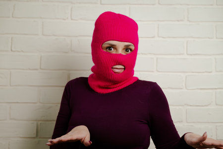 A woman wearing a bright pink balaclava dances energetically, striking unique poses with her hands...