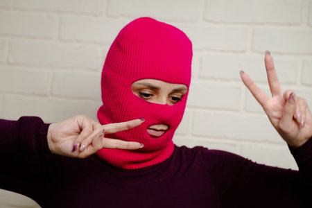 A woman wearing a bright pink balaclava dances energetically, striking unique poses with her hands...