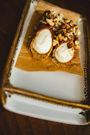 Two cannoli on a plate with. The cannoli are filled with cream and topped with nuts. The plate is a simple white ceramic plate with a brown borderの写真素材