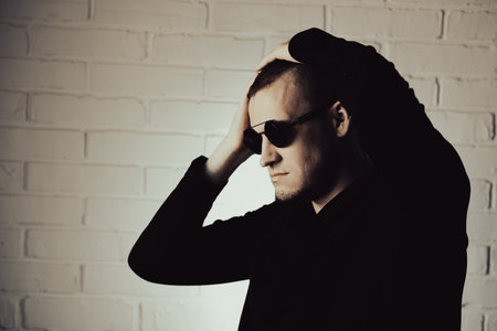 Man Posing Dramatically in Sunglasses Against White Brick Wall at Night.