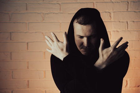 Man in Black Hoodie Performing Dance Moves Against White Brick Wall in Daylight