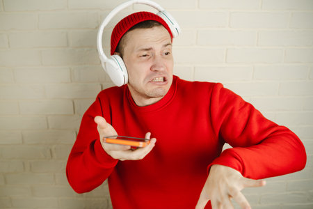 A man is wearing headphones and holding a cell phone in his hand. To be listening to music