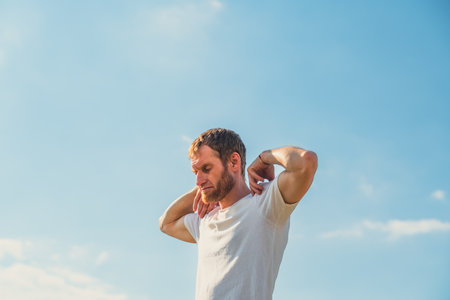 A professional sportsman is standing in front of a clear blue sky, engaging in shoulder and arm...