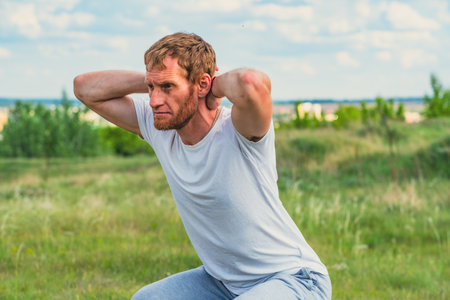 A professional sportsman is squatting in a field, with his hands behind his head. Male Performing...