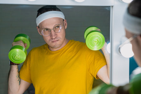 A man with glasses and a headband is lifting green dumbbells while standing in front of a vanity...