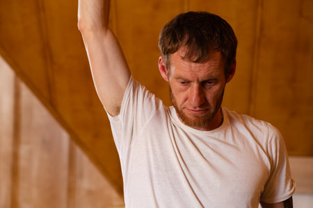 A man with beard is warming up his muscles before a workout. He is raising his right arm and...