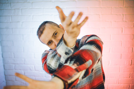 Man in Plaid Shirt Dancing in Front of a Brick Wall.