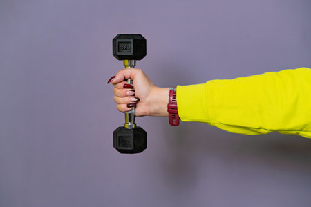 Woman in Yellow Hoodie Lifting dumbbell Against a Purple Wallの写真素材