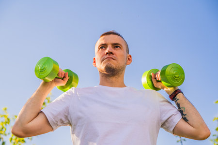 Man Lifting Green Dumbbells During Outdoor Workout in Sunny Day