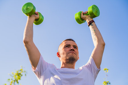 Man Lifting Green Dumbbells During Outdoor Workout in Sunny Day