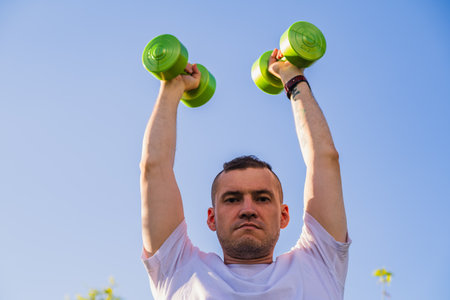 Man Lifting Green Dumbbells During Outdoor Workout in Sunny Day