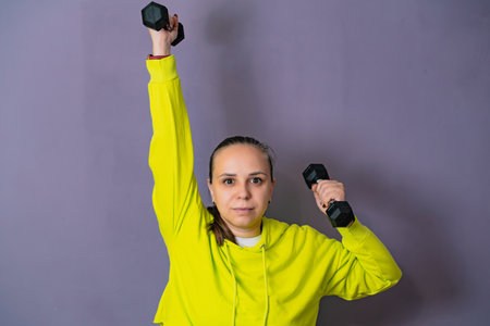 Woman in Yellow Hoodie Lifting dumbbell Against a Purple Wall
