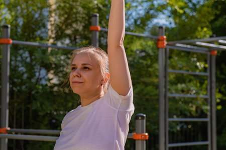 Woman performing a warm-up stretch routine in an outdoor setting. The exercise takes place on a...