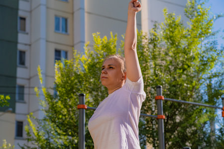 Woman performing a warm-up stretch routine in an outdoor setting. The exercise takes place on a...