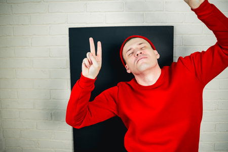 A man in a red hoodie and hat dances against a white brick wall.の写真素材