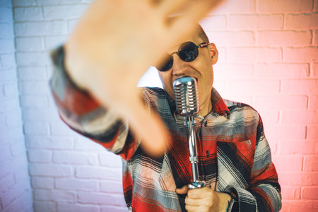 A man wearing a plaid shirt enthusiastically sings into a microphone, showcasing his passion for...
