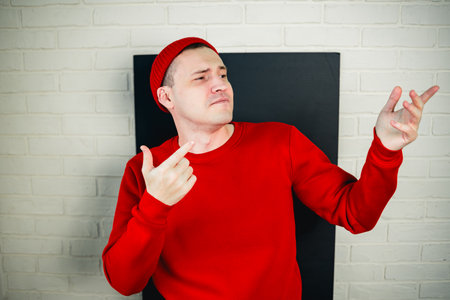 A man in a red hoodie and hat dances against a white brick wall.の写真素材