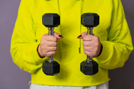 Woman in Yellow Hoodie Lifting dumbbell Against a Purple Wallの写真素材