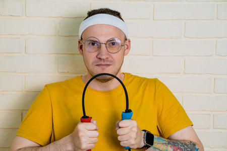A man with glasses and a headband is holding resistance bands in front of him. He is wearing a yellow t-shirt.の写真素材