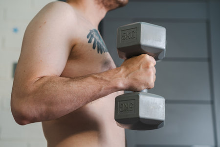 A shirtless man with a tattoo on his chest lifts a gray dumbbell.の写真素材