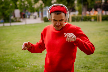 A Man In A Red Sweater Dances With Headphones On In A Park.の写真素材
