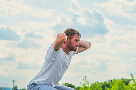 A professional sportsman is squatting in a field, with his hands behind his head. Male Performing...