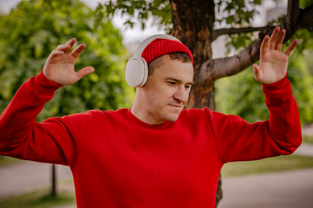 A Man In A Red Sweater Dances With Headphones On In A Park.