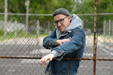 A Man with glasses in a Denim Jacket Dances Near a Chain Link Fence.の写真素材