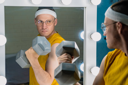 A man wearing a headband and glasses lifts a dumbbell in front of a vanity mirror.の写真素材