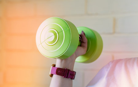 A woman lifts a green dumbbell with her right arm, while wearing a smartwatch and a white shirt.の写真素材