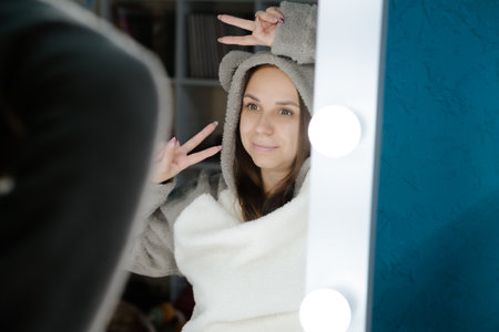 A young woman dances energetically in front of a mirror in her bedroom. Shes wearing a gray hoodie and smiling as she moves.の写真素材