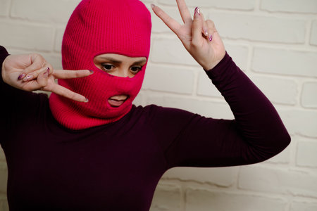 A woman wearing a bright pink balaclava dances energetically, striking unique poses with her hands against a clean, white brick wall background.の写真素材