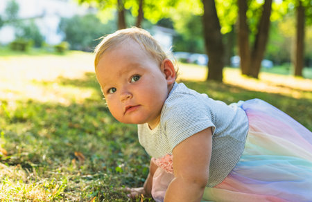 Baby Crawling on Green Grass in a Sunlit Park Surrounded by Trees.